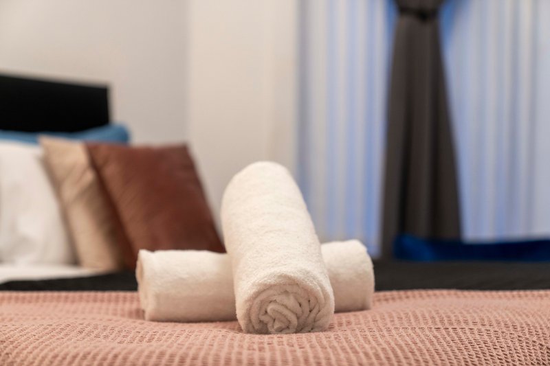 Rolled white towels arranged on bed with cushions and curtains in background