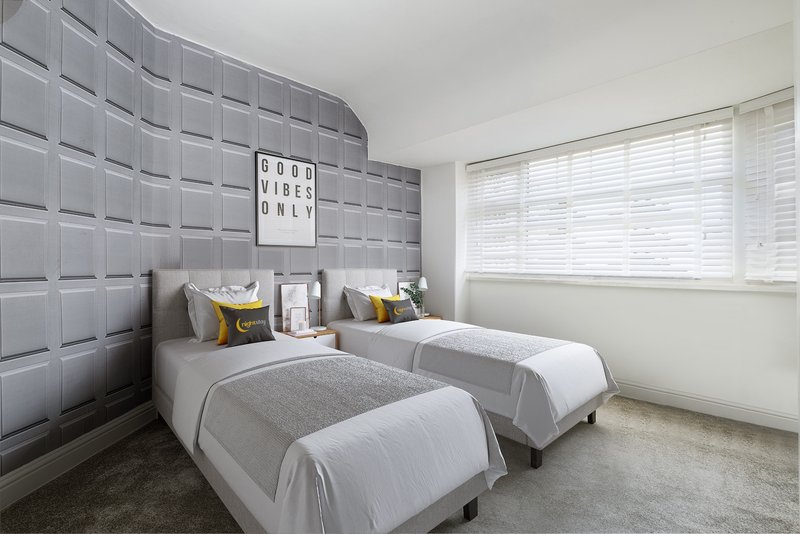 Modern bedroom with two single beds, gray padded headboard wall, and large window with blinds