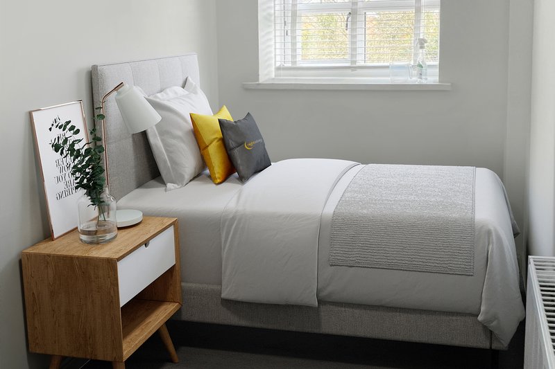 Bright bedroom with single bed, wooden nightstand, decorative pillows and window