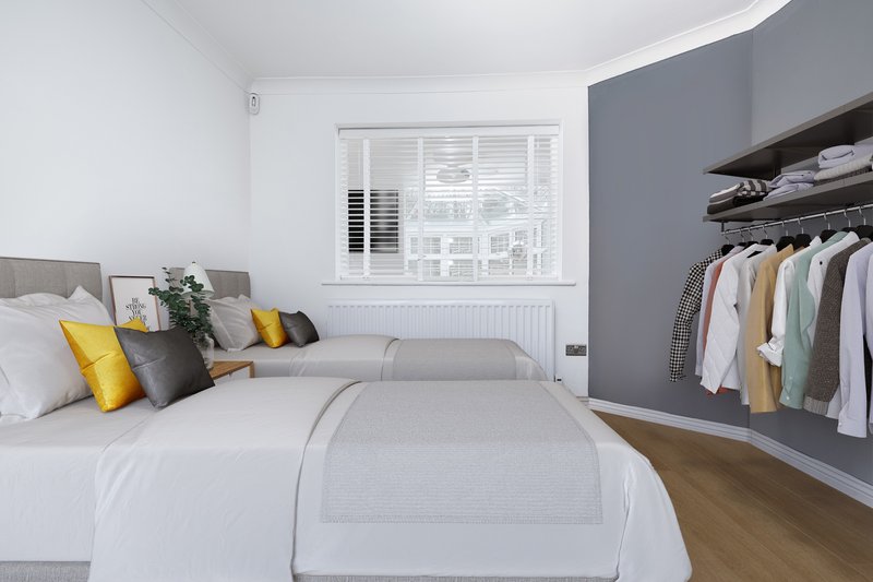 Modern bedroom with double bed, gray headboard, yellow accent pillows, open wardrobe and window
