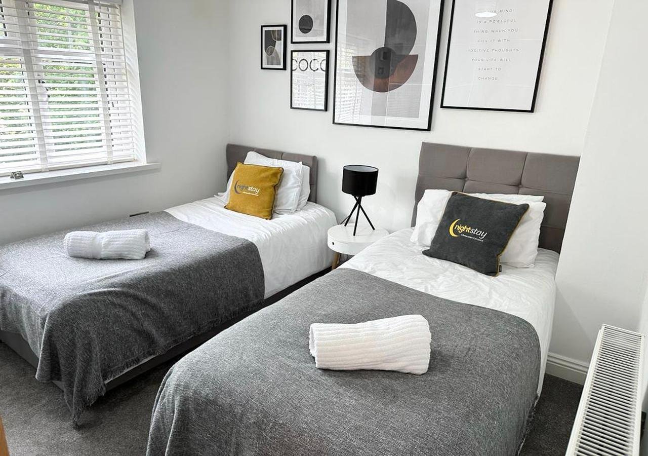 Modern bedroom with two single beds, grey upholstered headboards, white bedding and folded towels