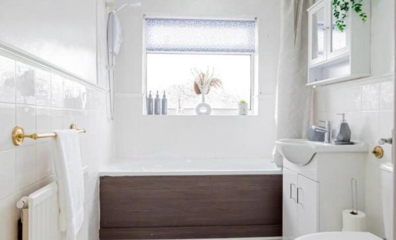 Clean bathroom with dark wood bathtub, white subway tile walls, window with blind and potted plant