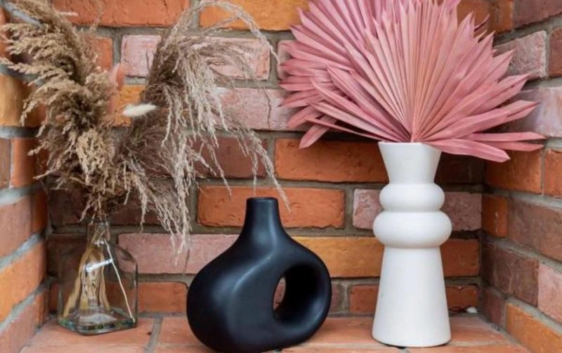 Brick fireplace shelf with dried pampas grass, black ceramic vase and white vase with pink dried palms