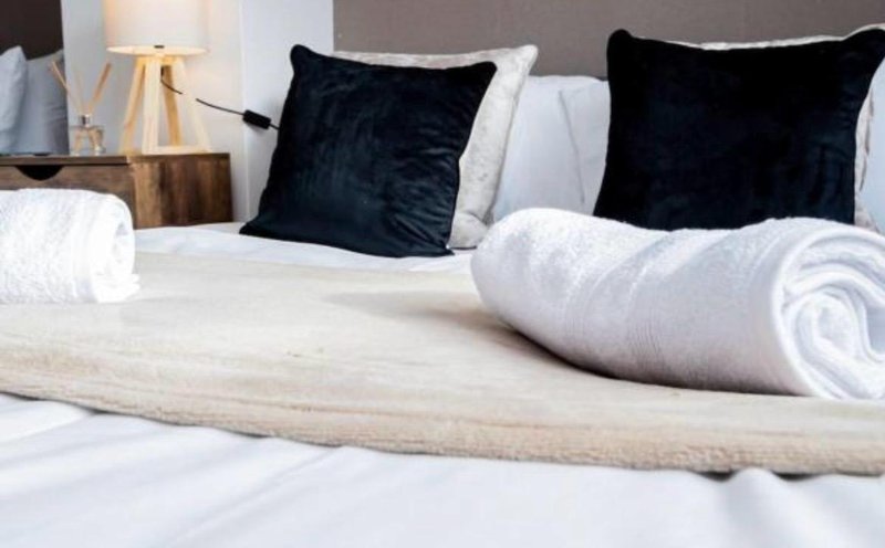 Bedroom with double bed, black velvet cushions, white bedding, rolled towels and wooden bedside table