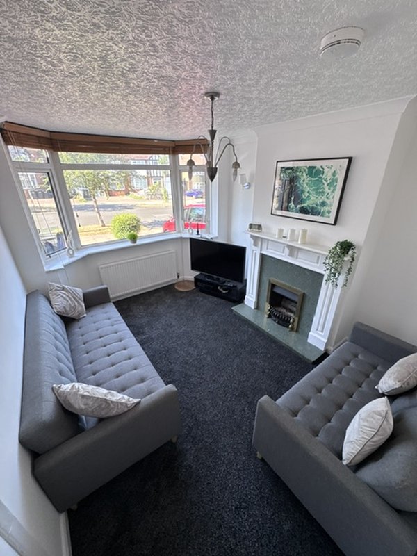 Modern living room with two grey sofas, fireplace, TV, and bay window overlooking street