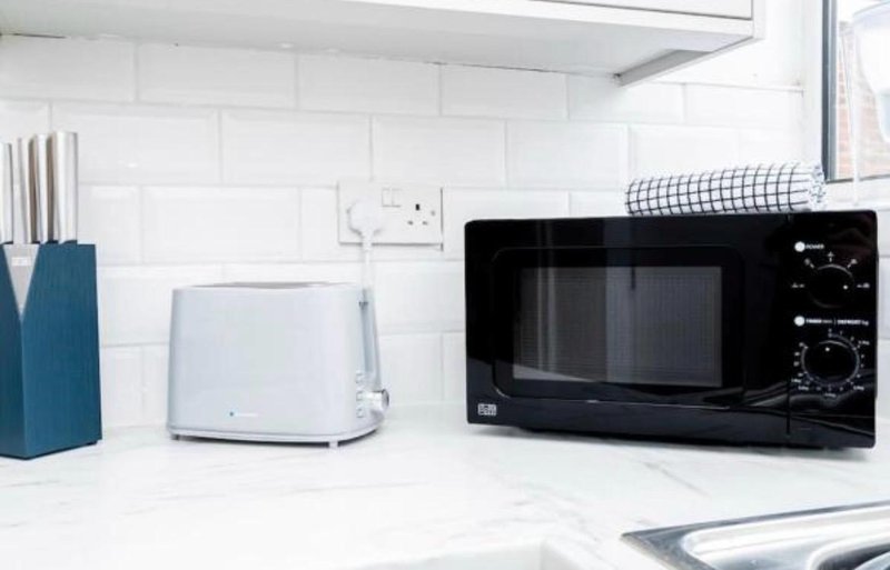 Modern white kitchen with black microwave, white toaster, and kitchen utensils on counter