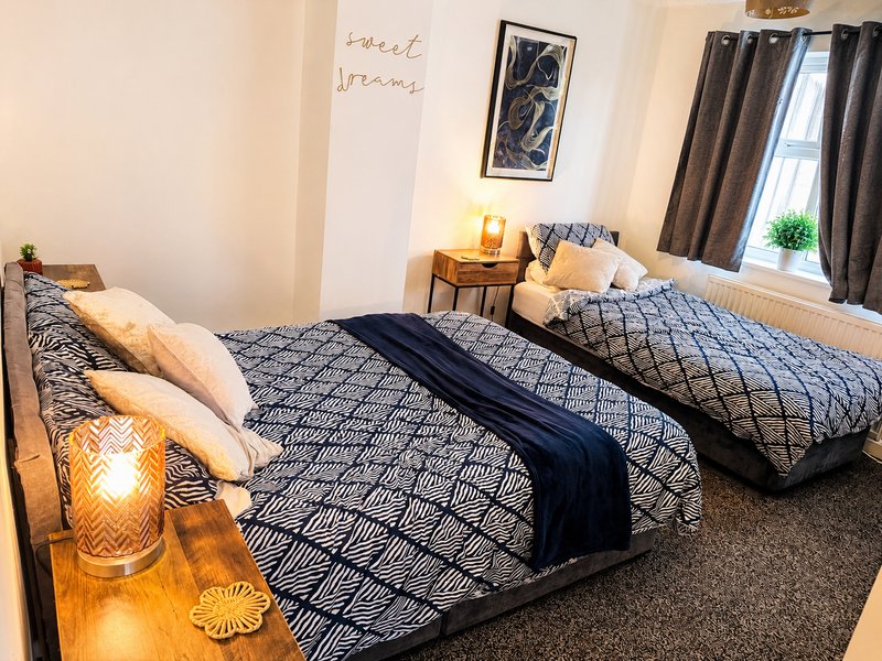 Bright bedroom with two single beds, patterned bedding, wooden nightstands, and window with curtains