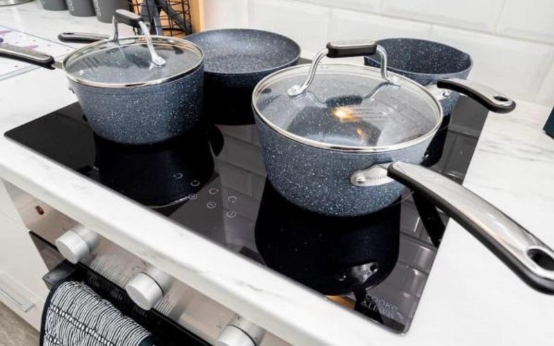 Kitchen stovetop with three granite cookpots and glass lids on induction hob