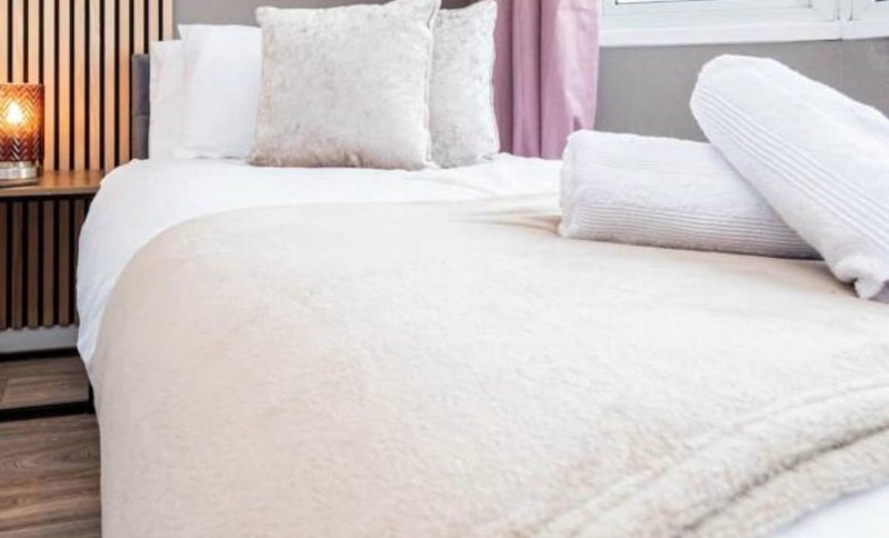Modern bedroom with white bedding, decorative pillows, wooden floor and bedside lamp