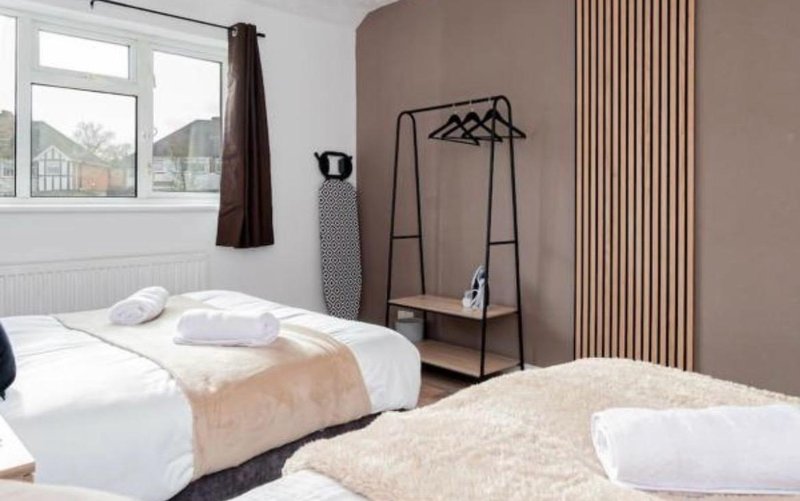 Bedroom with two beds, white bedding, clothing rack, and large windows with curtains