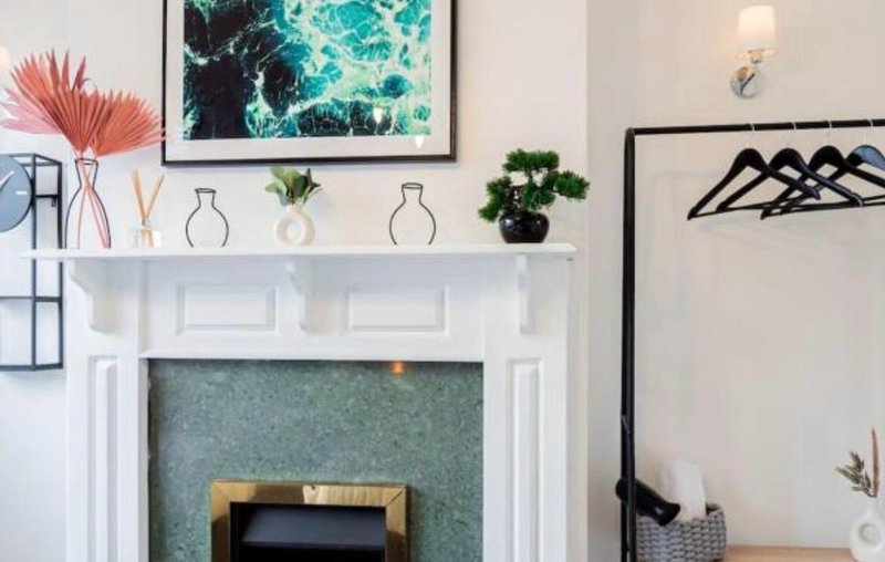Modern fireplace with white mantelpiece, decorative plants, framed artwork and wall sconces