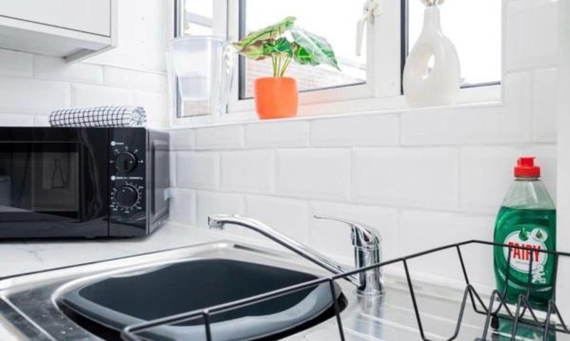 Modern kitchen with white subway tile backsplash, microwave, sink, and windowsill plants