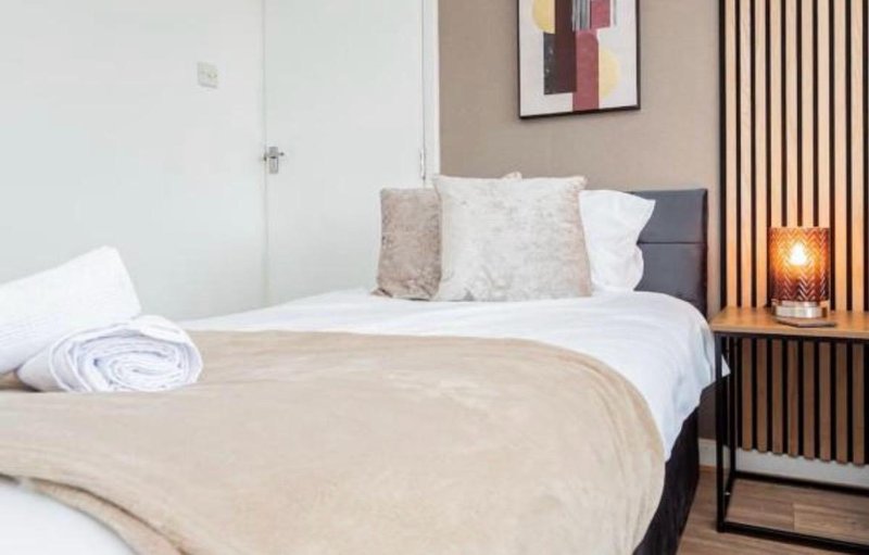 Modern bedroom with double bed, beige bedding, decorative pillows and wall art