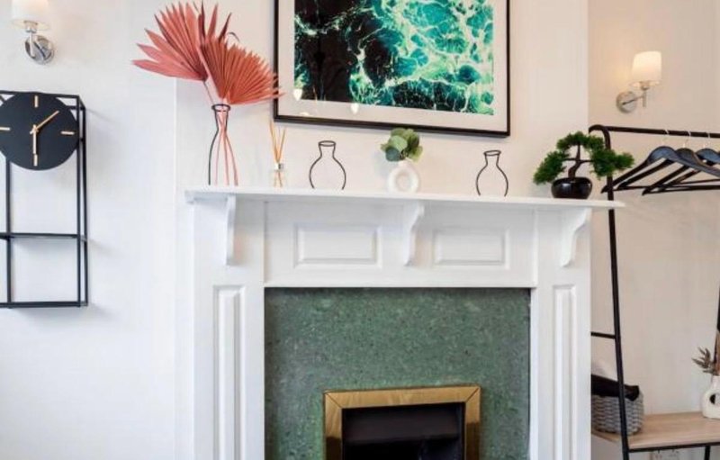 Living room with white fireplace mantel, decorative vases, pink dried flowers, and framed artwork above