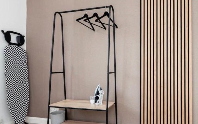 Modern bedroom with black metal clothing rack, wooden shelf, and geometric wall decor