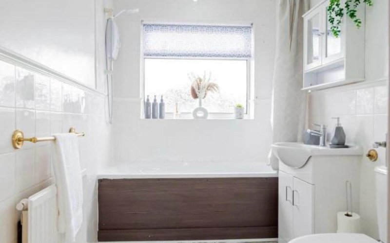 Modern bathroom with dark wood bathtub, white subway tile, window with plant, and brass fixtures