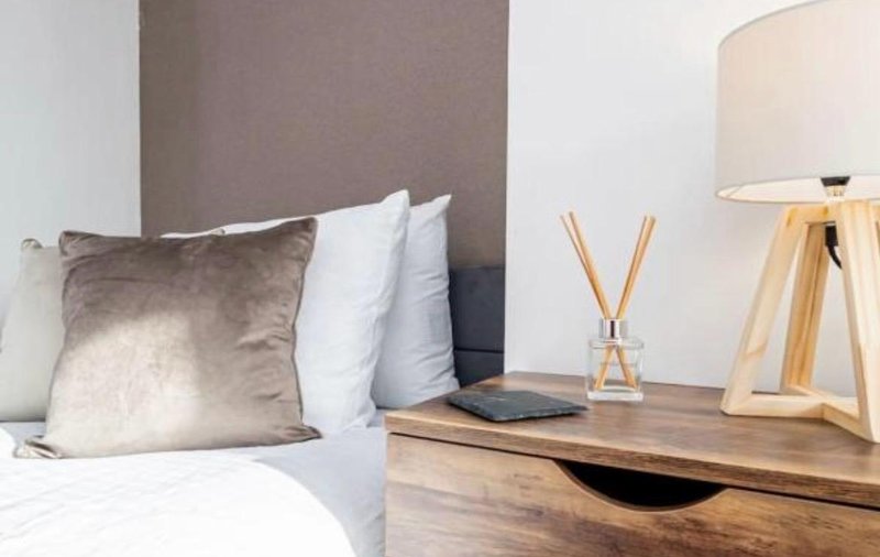 Bedroom with double bed, decorative pillows, wooden nightstand, and table lamp