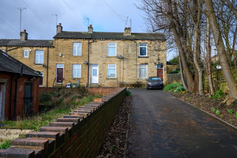 Stone terraced house with driveway, parked car, bare trees and brick wall