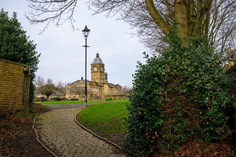 Stone church with clock tower visible across green grounds and paved pathway