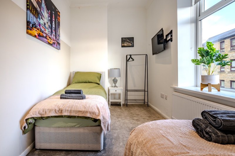 Bright bedroom with two single beds, green bedding, wall art, and large window with city view