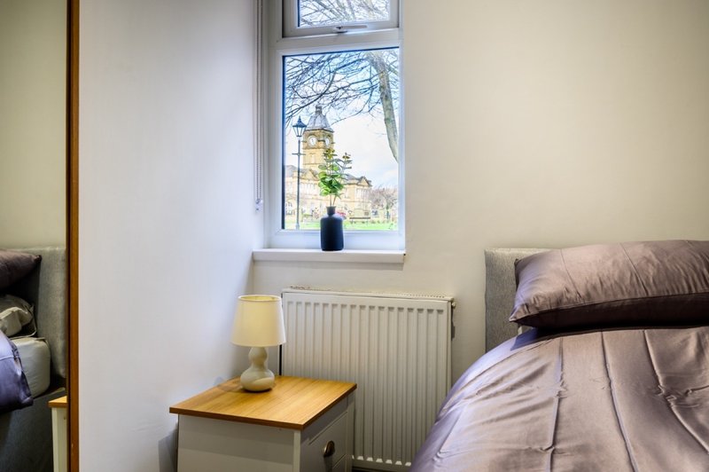 Bedroom with single bed, bedside table, lamp, radiator and window overlooking street
