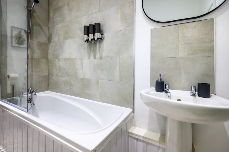 Modern bathroom with white bathtub, beige tiles, pedestal sink and mirror