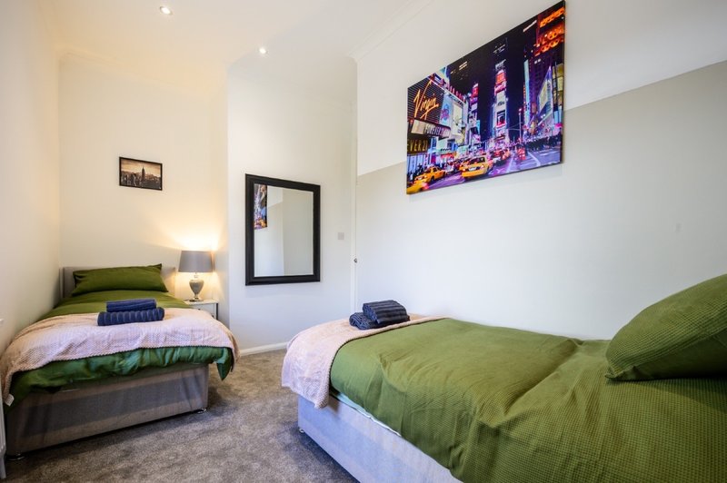 Shared bedroom with two single beds, green bedding, wall art, and desk lamp