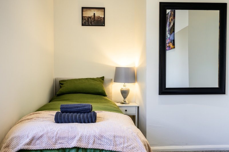 Bedroom with single bed, green pillow, white bedding, bedside lamp and mirror