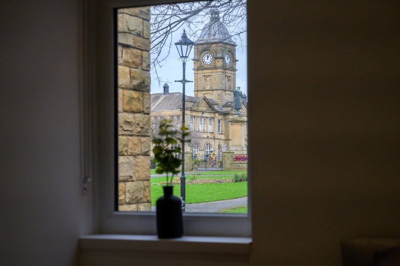 Interior window view showing historic stone building with clock tower and green lawn outside