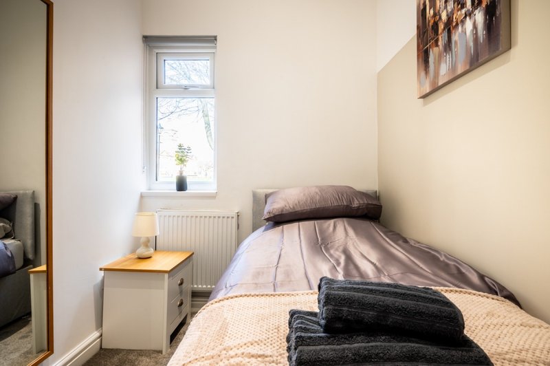 Compact bedroom with single bed, wooden bedside table, radiator and small window