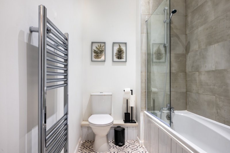 Modern bathroom with toilet, bathtub, heated towel rail and botanical wall art