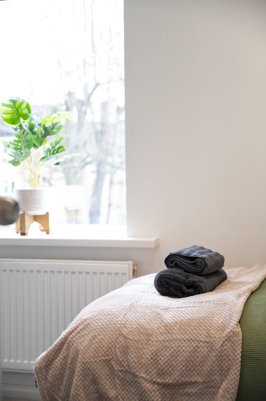 Bright bedroom with bed, folded towels, radiator and potted plant by window