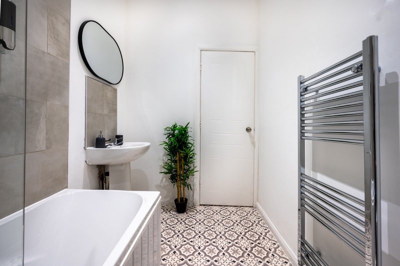 Modern bathroom with white bathtub, pedestal sink, heated towel rail and patterned floor tiles