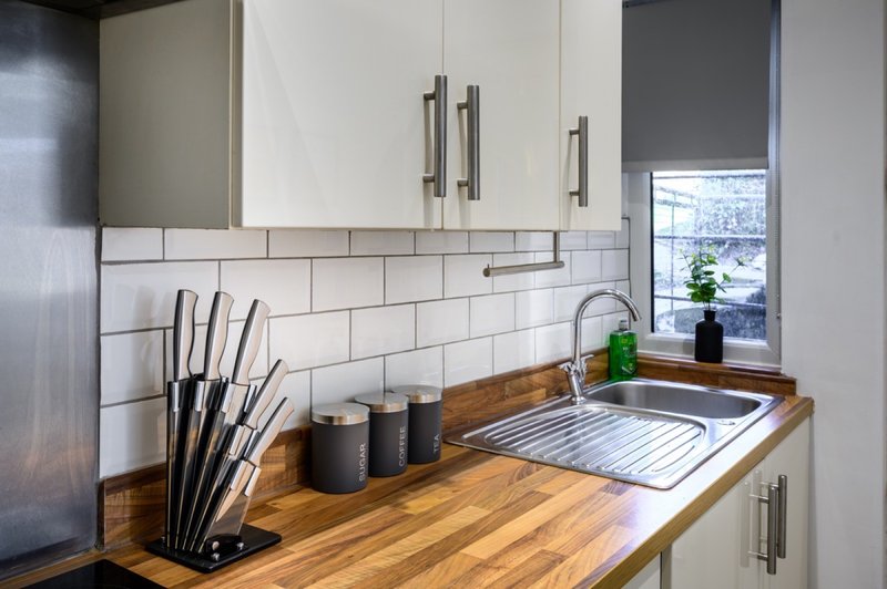Modern kitchen with white cabinetry, subway tile backsplash, wooden countertop and stainless steel sink