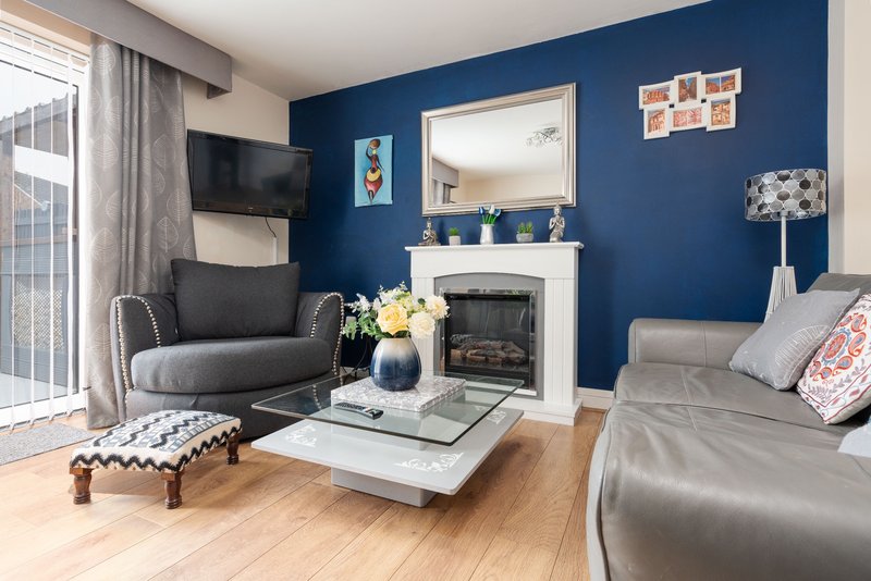 Modern living room with blue accent wall, fireplace, grey furniture, and wooden flooring