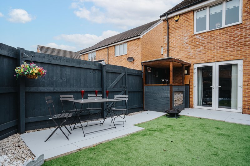 Modern brick house with patio area, dining table, dark fence, and manicured garden
