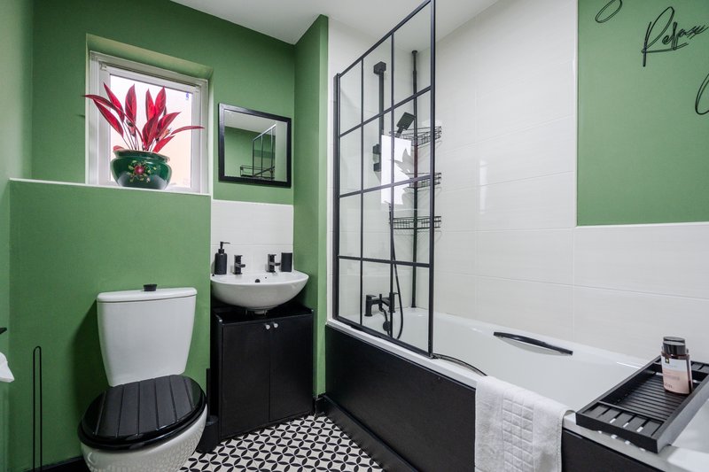 Modern bathroom with green and white walls, black and white tile floor, toilet, sink and shower