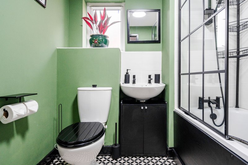 Modern bathroom with green walls, toilet, black sink vanity, shower enclosure and potted plant