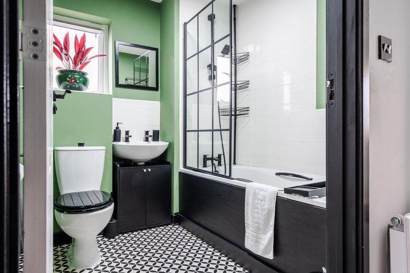 Modern bathroom with green walls, black and white tile floor, toilet, sink and shower enclosure
