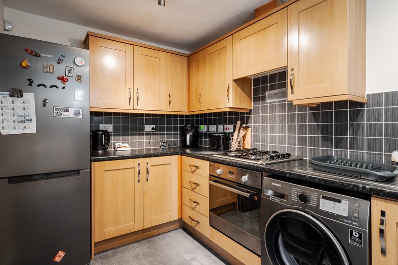 Kitchen with wooden cabinets, black tiled backsplash, gas hob, oven and washing machine