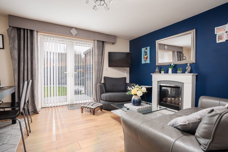 Open-plan living room with fireplace, blue accent wall, leather sofa, and patio doors