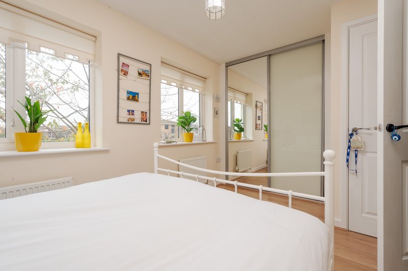 Bright bedroom with white bed, mirrored wardrobe, windows and potted plants on sill