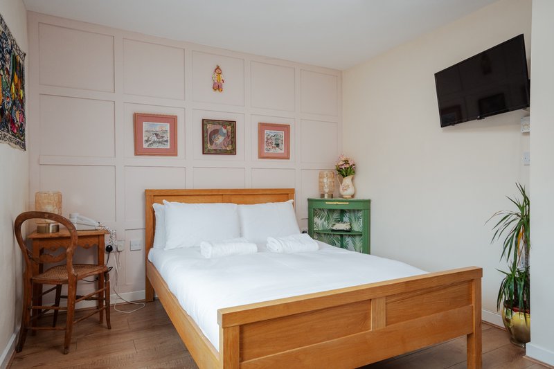 Bright bedroom with wooden bed, white bedding, wall-mounted TV, and potted plant