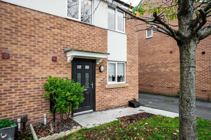 Modern brick townhouse exterior with black front door, paved courtyard, and mature tree