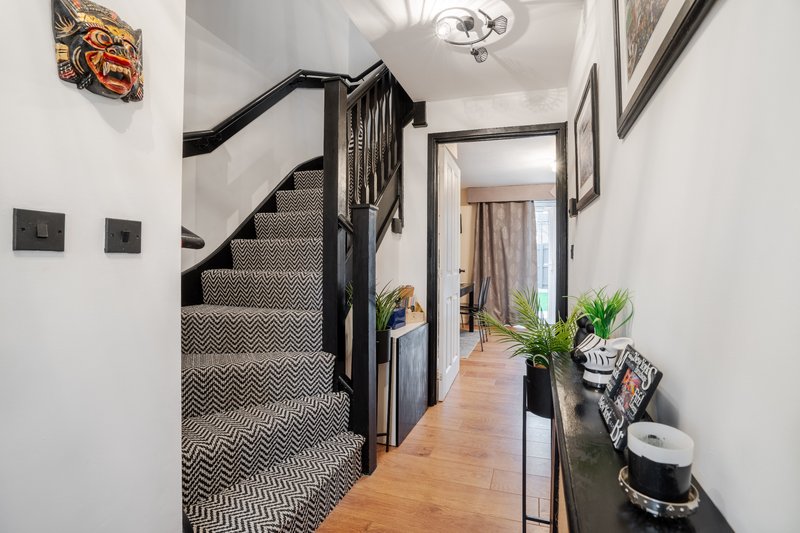 Modern hallway with wooden floor, black staircase, white walls and decorative items on shelf