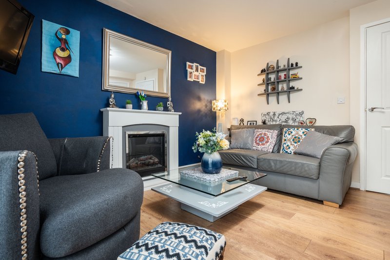 Modern living room with blue accent wall, fireplace, gray sofa and armchair, wooden floor