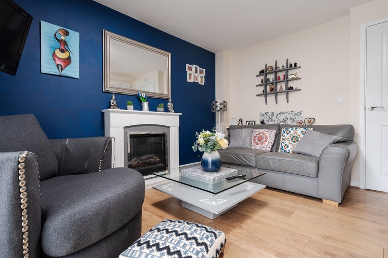 Living room with gray upholstered furniture, fireplace, blue accent wall, and wooden floor