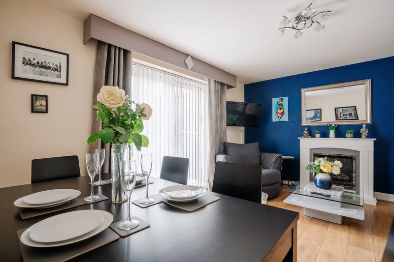 Open-plan dining and living room with black table, blue accent wall, fireplace and contemporary furnishings