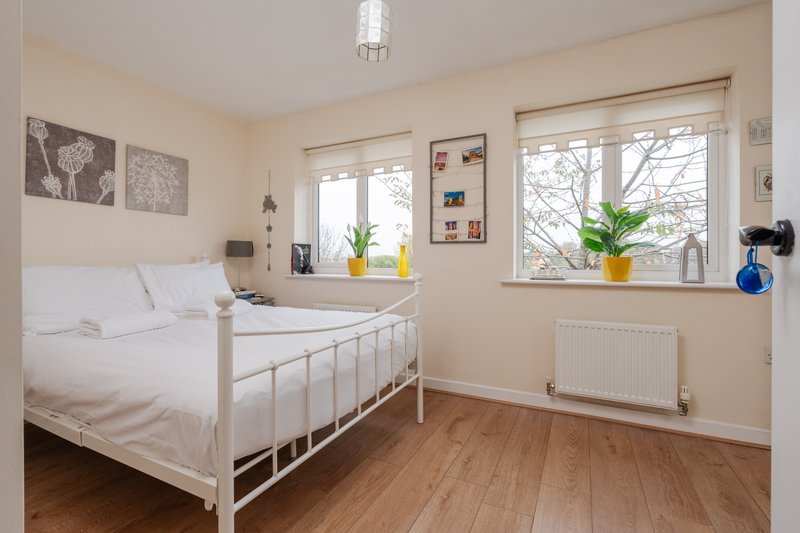 Bright bedroom with white metal bed frame, wooden floor, large windows and wall art