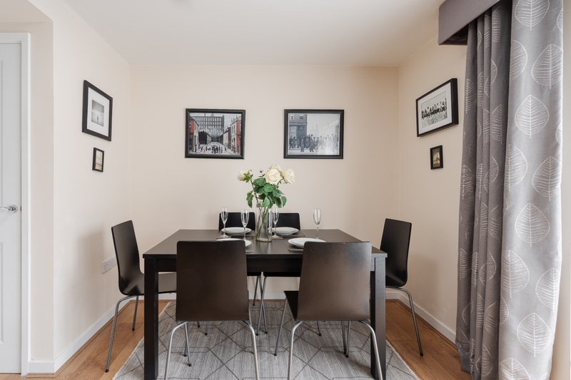 Dining room with black table, four chairs, framed artwork and potted flowers